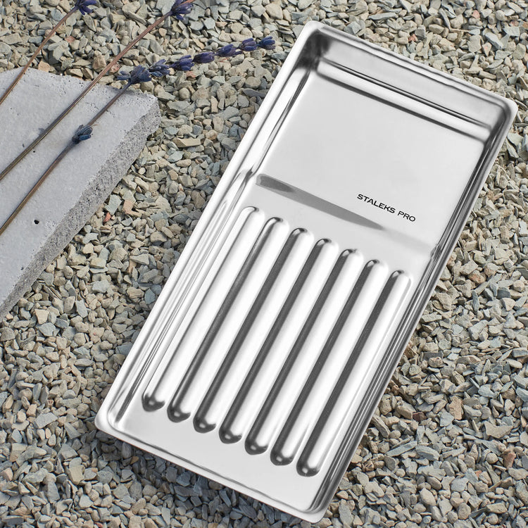 Plateau à outils Staleks Pro en acier inoxydable posé sur graviers, accessoire professionnel pour la manucure et la pédicure.