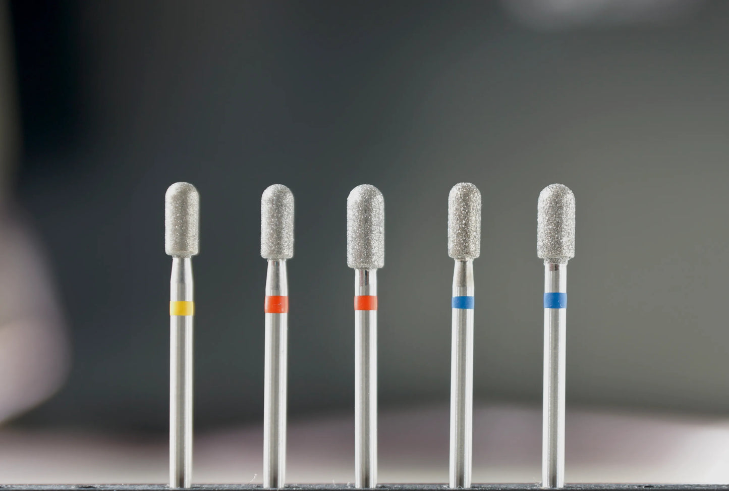 Ensemble de six fraises en diamant de forme cylindre arrondi, classées par granulométrie (jaune, rouge, bleu), destinées aux soins des ongles et au travail de surface en manucure et pédicure.
