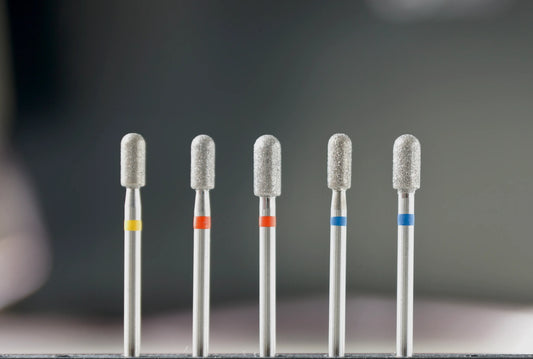 Ensemble de six fraises en diamant de forme cylindre arrondi, classées par granulométrie (jaune, rouge, bleu), destinées aux soins des ongles et au travail de surface en manucure et pédicure.