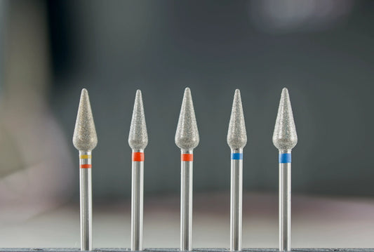 Vue rapprochée de cinq fraises en diamant de forme tulipe, classées par granulométrie (jaune, rouge, bleu), utilisées pour le soin des cuticules et des ongles naturels.