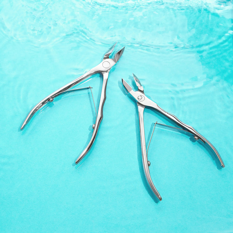 Deux pinces professionnelles Staleks en acier inoxydable posées sur fond bleu, outils de précision pour manucure et pédicure.