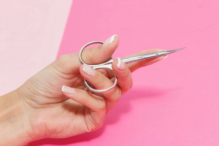 Ciseaux Staleks en acier inoxydable tenus en main sur fond rose, outil professionnel pour manucure et pédicure.